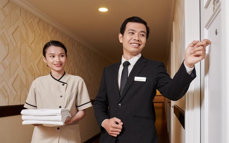 Hotel manager knocking on door, maid waiting beside him, room service concept