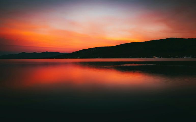 Silhouette of Mountains near Calm Lake during Sunset