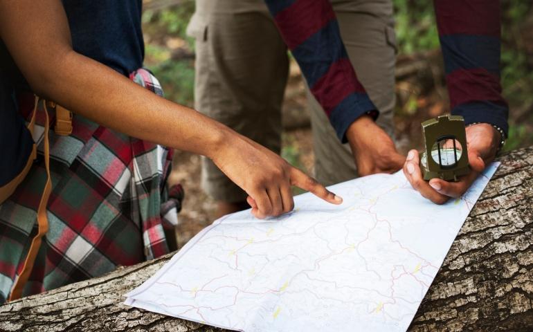 Two people are using a map and compass to navigate in a forest