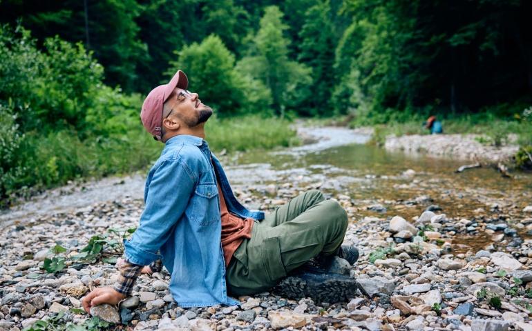 Young man relaxing by the creek while hiking in nature