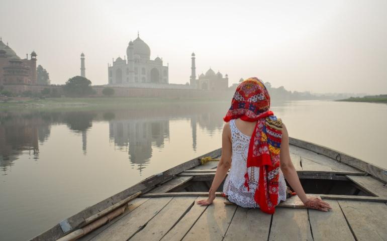A young woman watching the sunset over the Taj Mahal from a wooden boat
