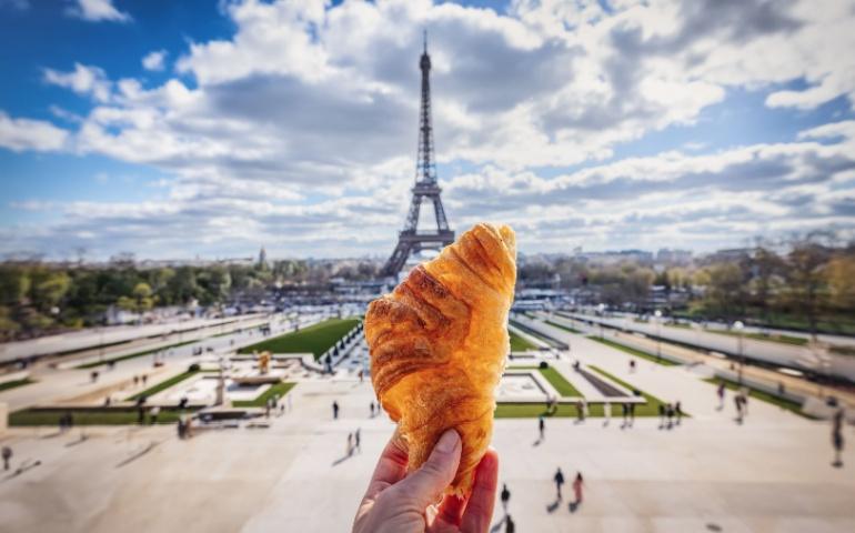 A tourist holding a French Croissant in front of the Eiffel Tower in Paris