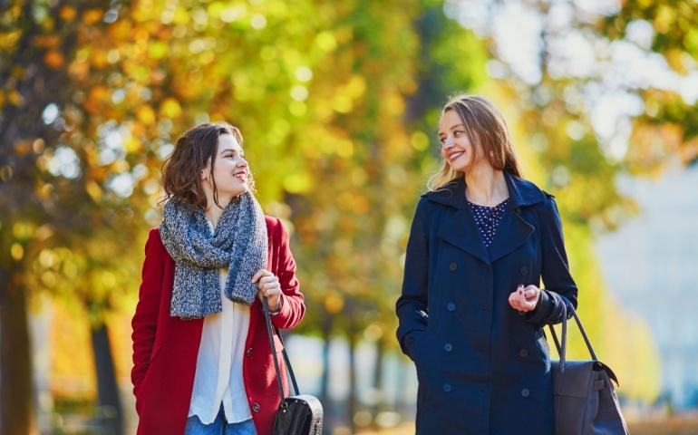 Two young girls walking in autumn park on sunny fall day, France