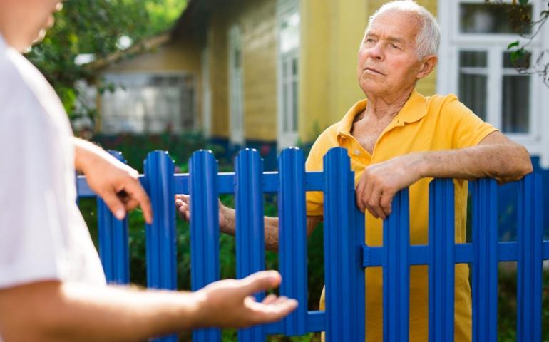 Old man talking with his neighbour beside fence of country house, France
