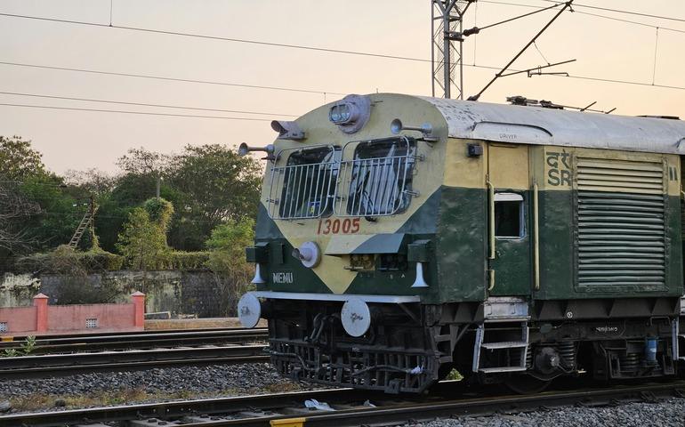 A green and yellow train travelling down tracks in Tamil Nadu