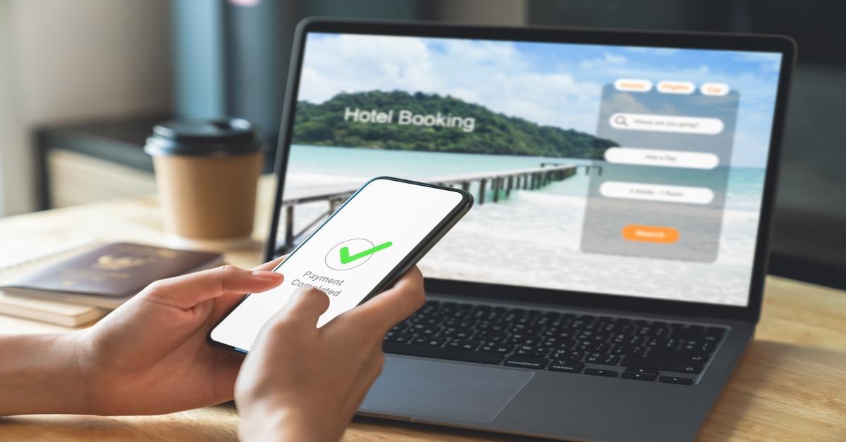Hand using laptop and booking hotel on website for vacation after a long work and payment completed message on mobile, Summer holiday concept.