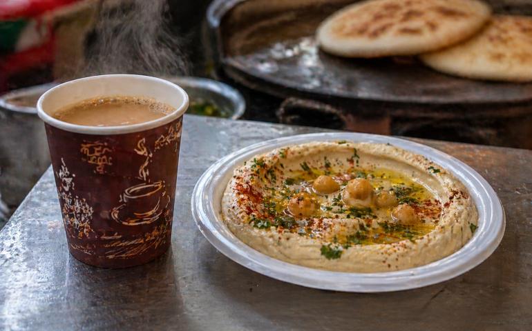 A close-up of a steaming cup of Karak tea and a plate of hummus from a local street vendor.