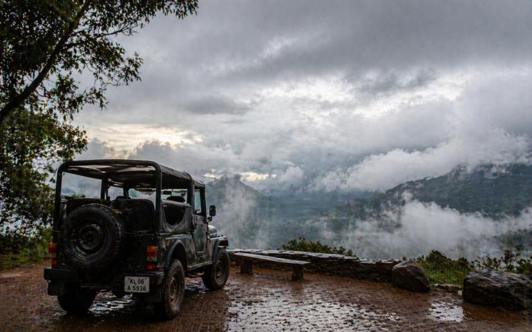 A jeep parked near a viewpoint with clouds rolling in