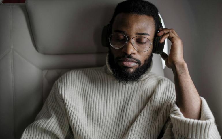 A man in a sweater enjoys music with headphones while sitting on an airplane