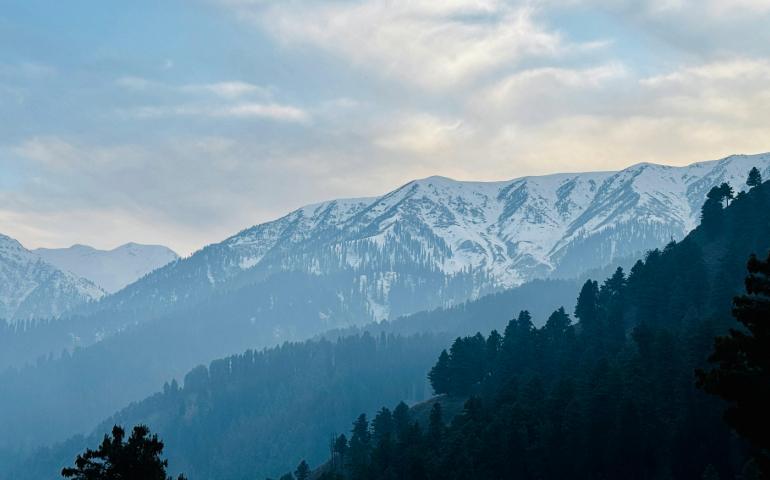 Breathtaking View of Snow-Covered Mountains in Gulmarg, Kashmir Against a Bright Sky.
