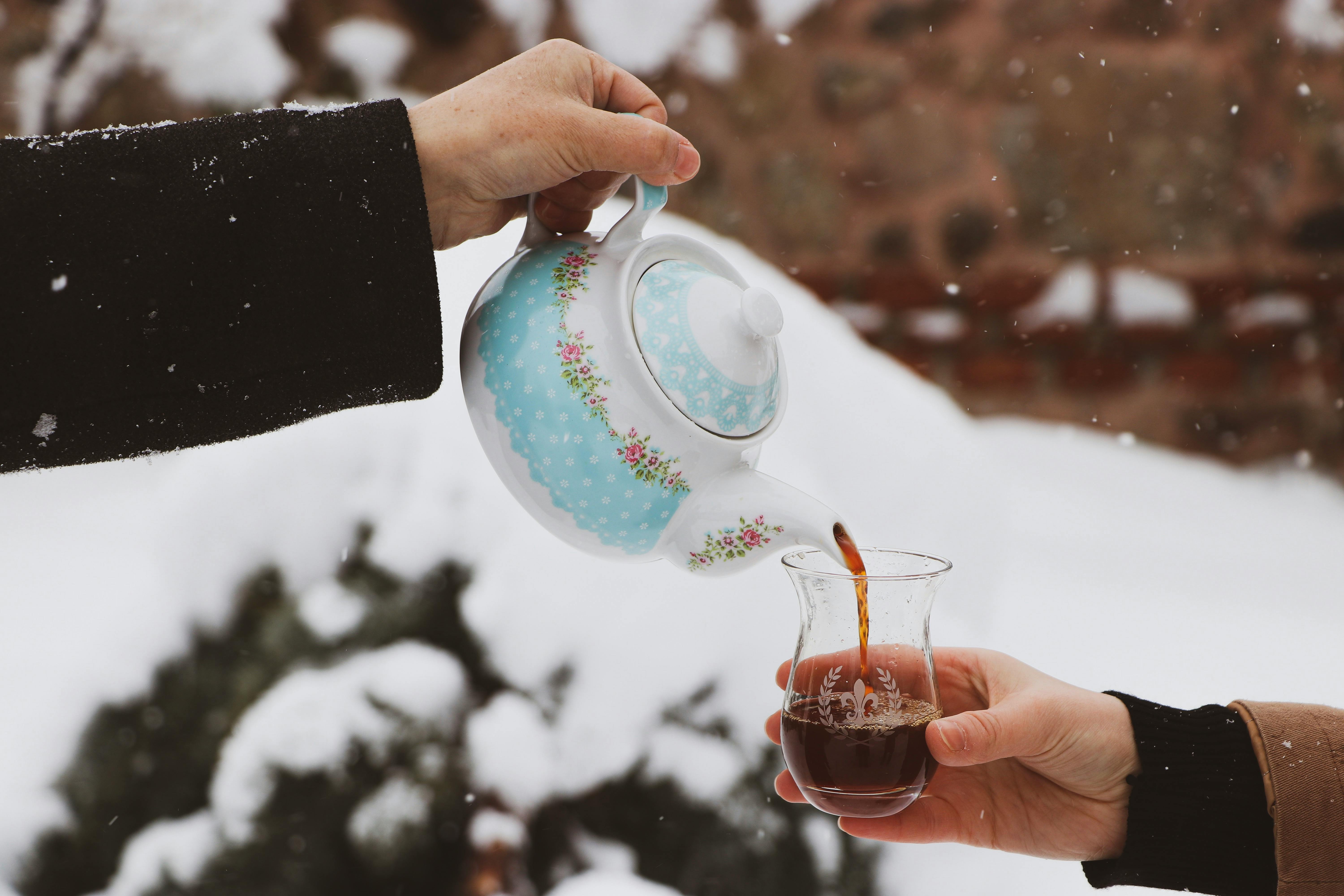 Close-up of Hands Pouring Tea From a Floral Teapot Into a Glass