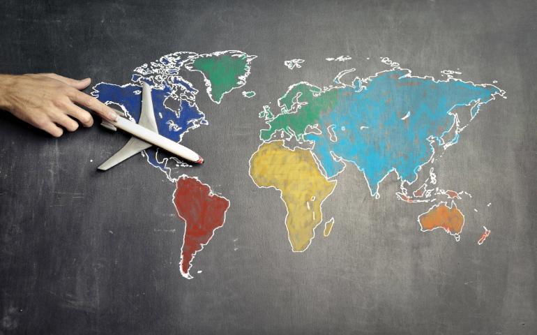 A hand guides a toy airplane over a colorful world map, symbolizing travel and exploration.