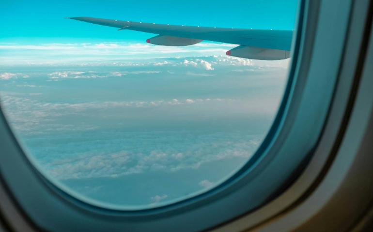 View From an Airplane Window Showing a Wing Above the Clouds With Blue Sky.