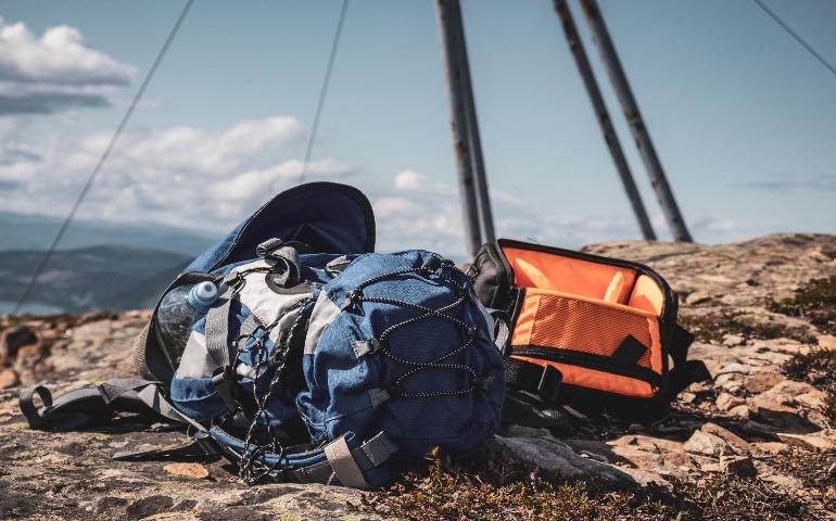 Blue and Orange Backpacks Resting on a Rocky Mountain Peak Under a Clear Sky