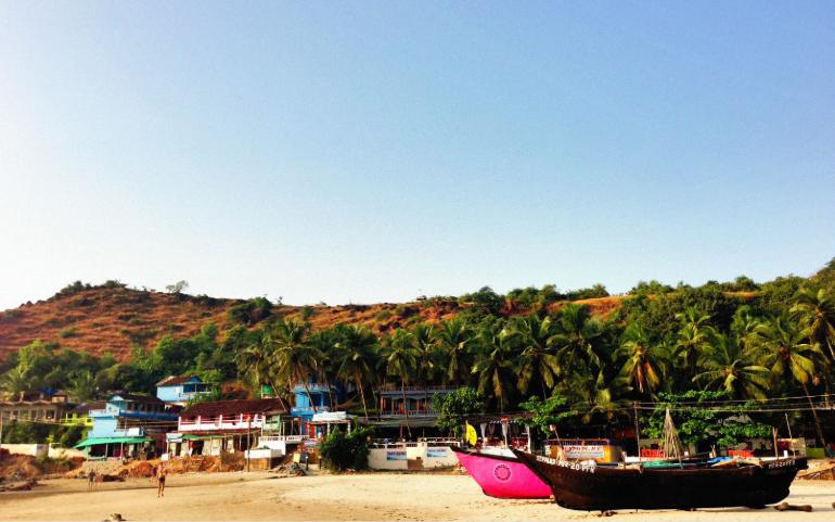Scenic sandy beach with vibrant boats, palm trees, and hillside backdrop.