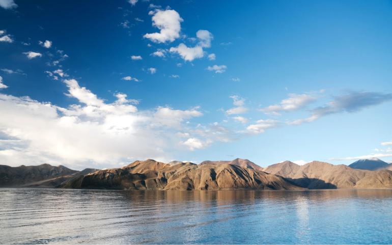 Landscape Featuring Calm lake Waters and Majestic Mountains Beneath a Vibrant Blue Sky.
