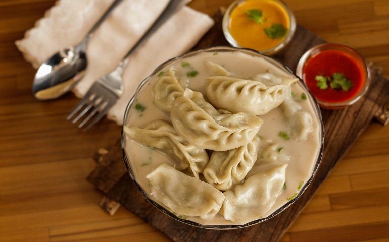 Momo served in savory broth with vibrant sauces.