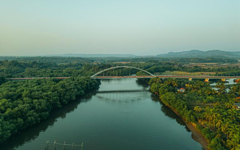 View of a bridge over a river surrounded by lush greenery in Aldona, Goa, India.