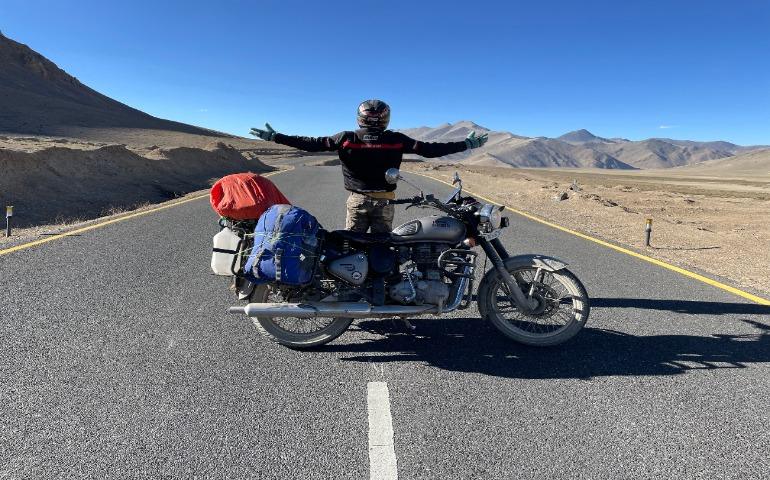Motorcyclist stands on an empty road in Leh.