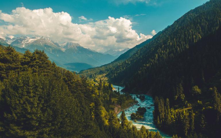 View of a River Flowing Through a Lush Green Forest Valley with Majestic Mountains