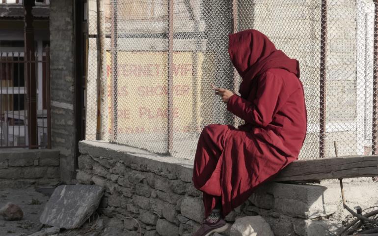 A woman in a red robe sits outdoors, using a smartphone, against an urban backdrop.