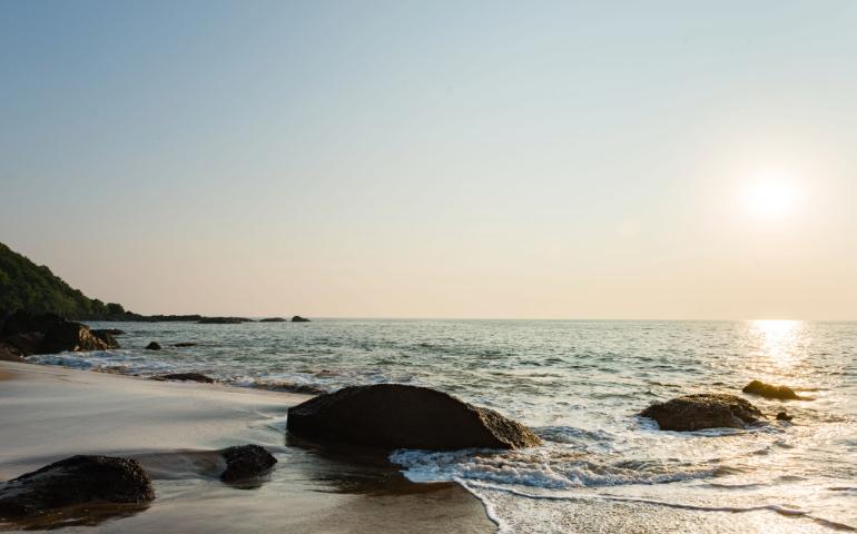 Peaceful beach view with rocks and gentle waves under a warm sunset sky of Goa