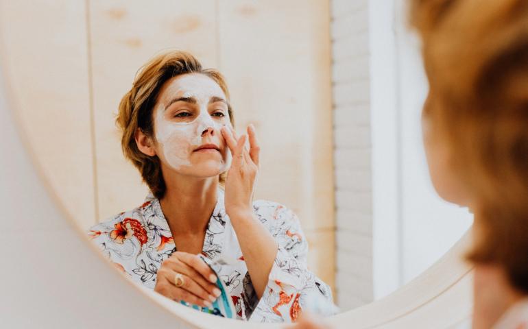 A woman applying a mask for skincare in front of a mirror
