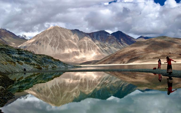 View of mountains and their reflection in Pangong Lake with people in the scene