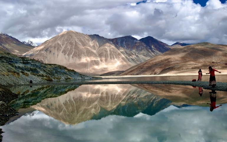 View of mountains and their reflection in Pangong Lake with people in the scene.