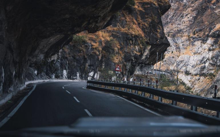Curved Road Through a Dramatic Mountain Pass Under Rocky Overhang.