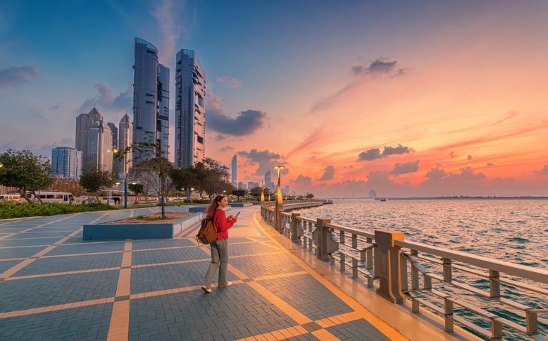 A tourist walking along the Abu Dhabi Corniche promenade at sunset