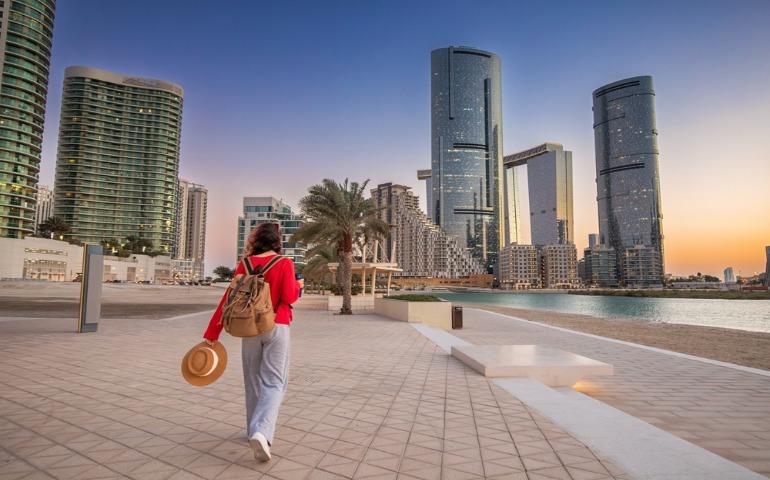A tourist walking at Reem island at sunset with skyscrapers and palm trees in background, Abu Dhabi