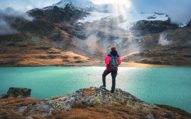 Young woman hiker with backpack standing on a rock with view on turquoise Alpine lake