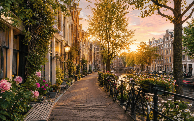 Amsterdam canal street with charming Dutch houses, bicycles, flowers, and golden-hour light