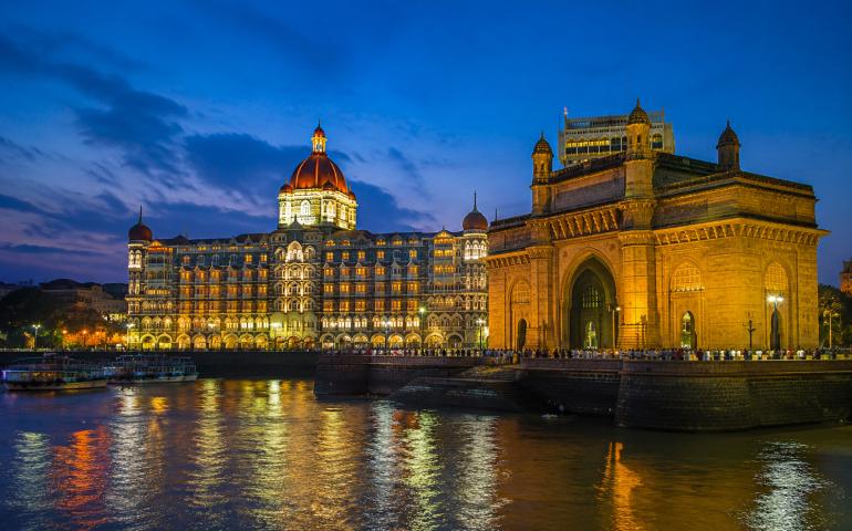 Taj Mahal Tower glowing beside the Gateway of India at blue hour — very Mumbai, very dramatic.”