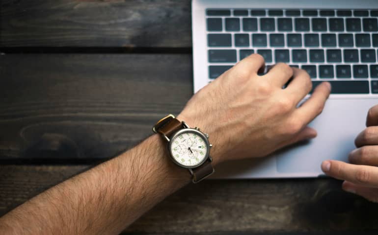 A person looking at his watch and using his laptop
