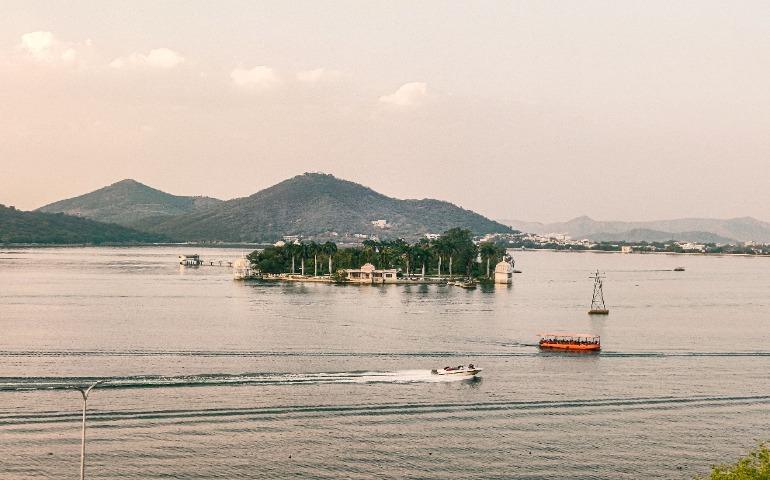 A serene aerial view of Lake Pichola with boats and hills in Udaipur, India.