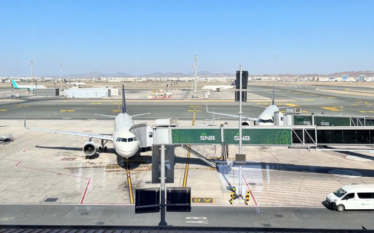 Airplane docked at terminal gate in Jeddah Airport, clear blue sky.