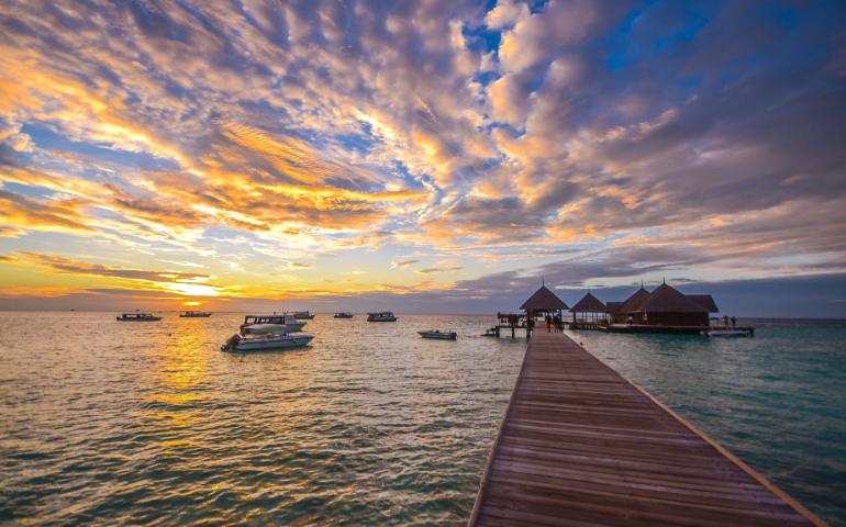 View of a tropical jetty surrounded by boats at sunset with vibrant skies