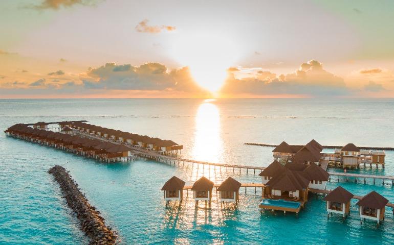 View of luxurious Maldives overwater villas at sunrise, perfect for a serene vacation.
