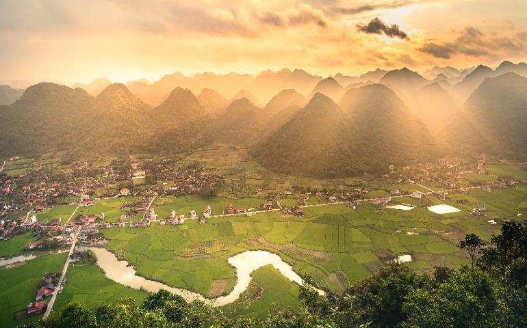 View of lush rice fields and limestone mountains at sunrise enveloped in golden light in Vietnam