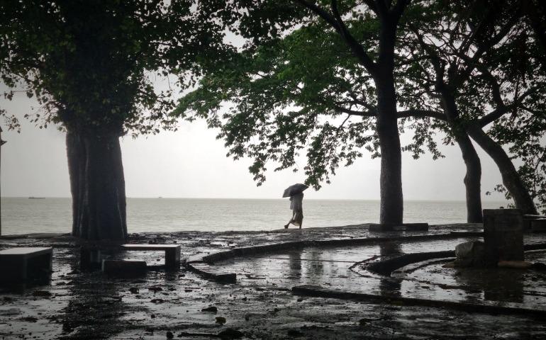 A person walks along a seafront path under rain, holding an umbrella