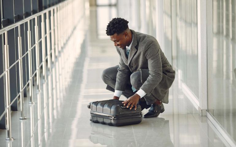 Confident businessman organizing suitcase in a bright airport corridor.