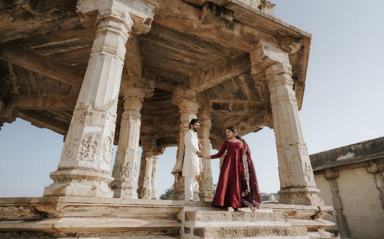 Couple standing at historic pavilion with intricate stone carvings, holding hand.