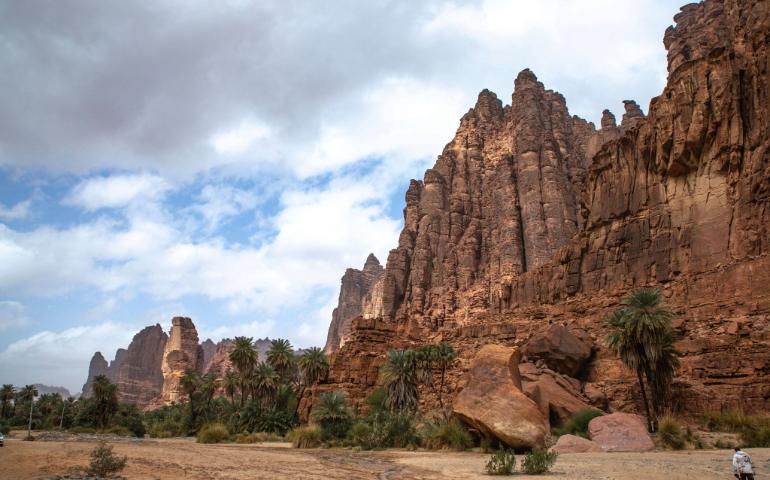 Towering rock formations against a cloudy sky and lush palm trees.