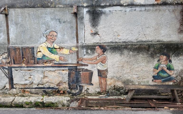 Charming street art mural depicting an elderly vendor and children on a Penang wall, Malaysia