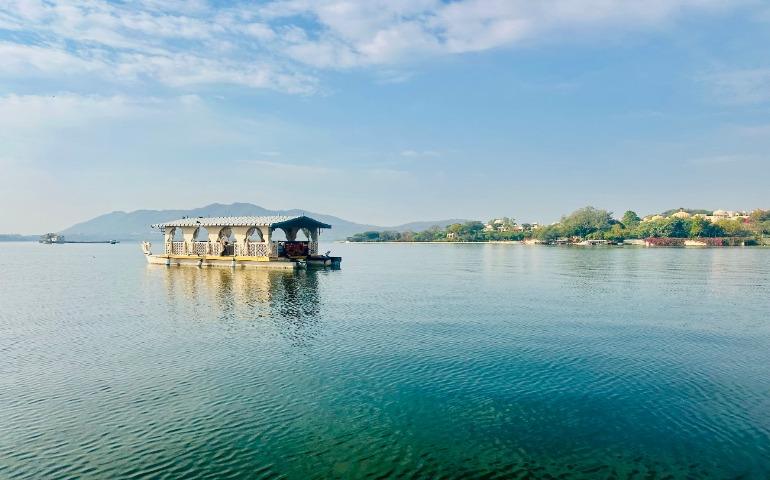 View of a serene houseboat on Lake Pichola with mountains in Udaipur, India.