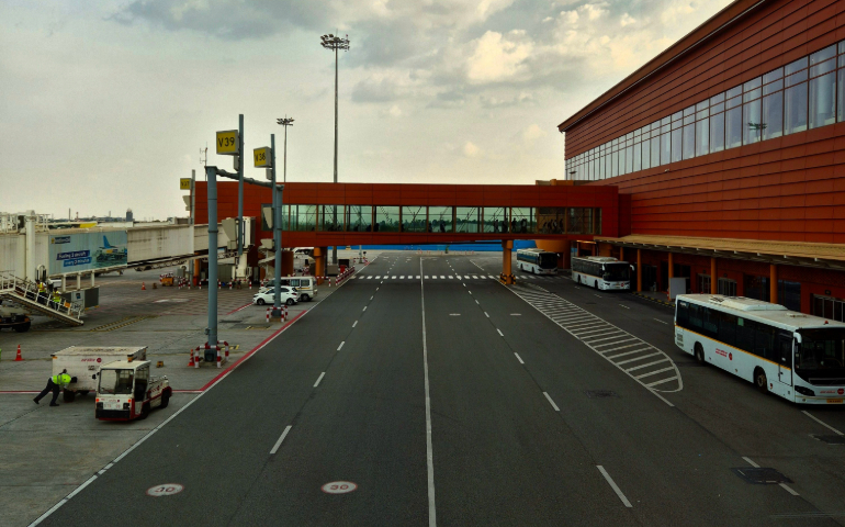 A bustling airport tarmac with terminal and buses under a cloudy sky.