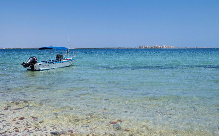 Beach scene with a moored motorboat on a clear blue sea under a sunny sky in Umluj
