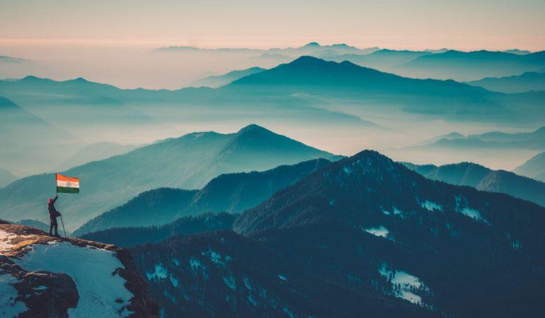An Indian flag stands atop a snowy mountain overlooking a misty Himalayan valley
Sanket Barik/Pexels